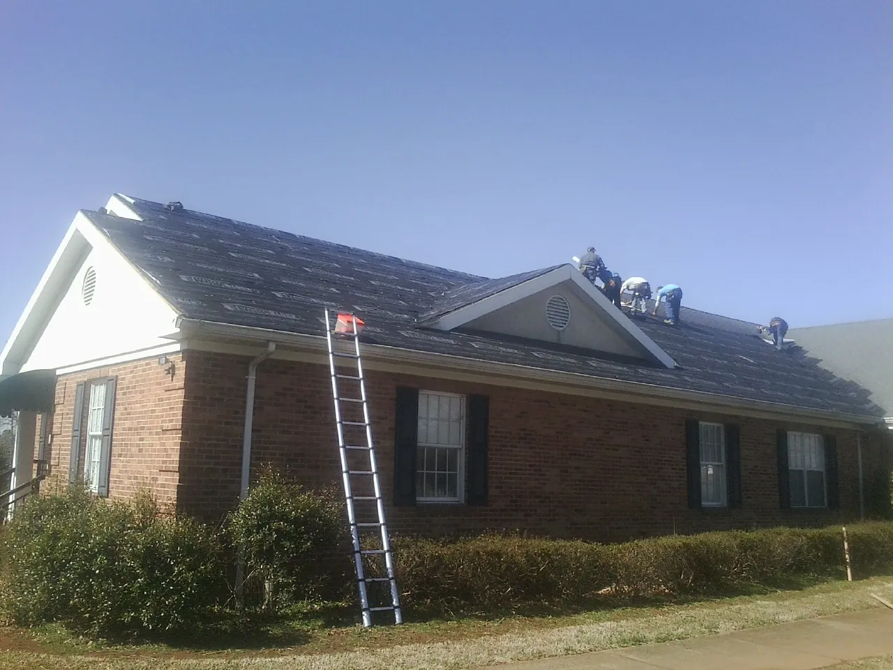 Crew tearing shingles off a brick ranch roof with a ladder set — Metal Roof Repair work by our crew in Cassville