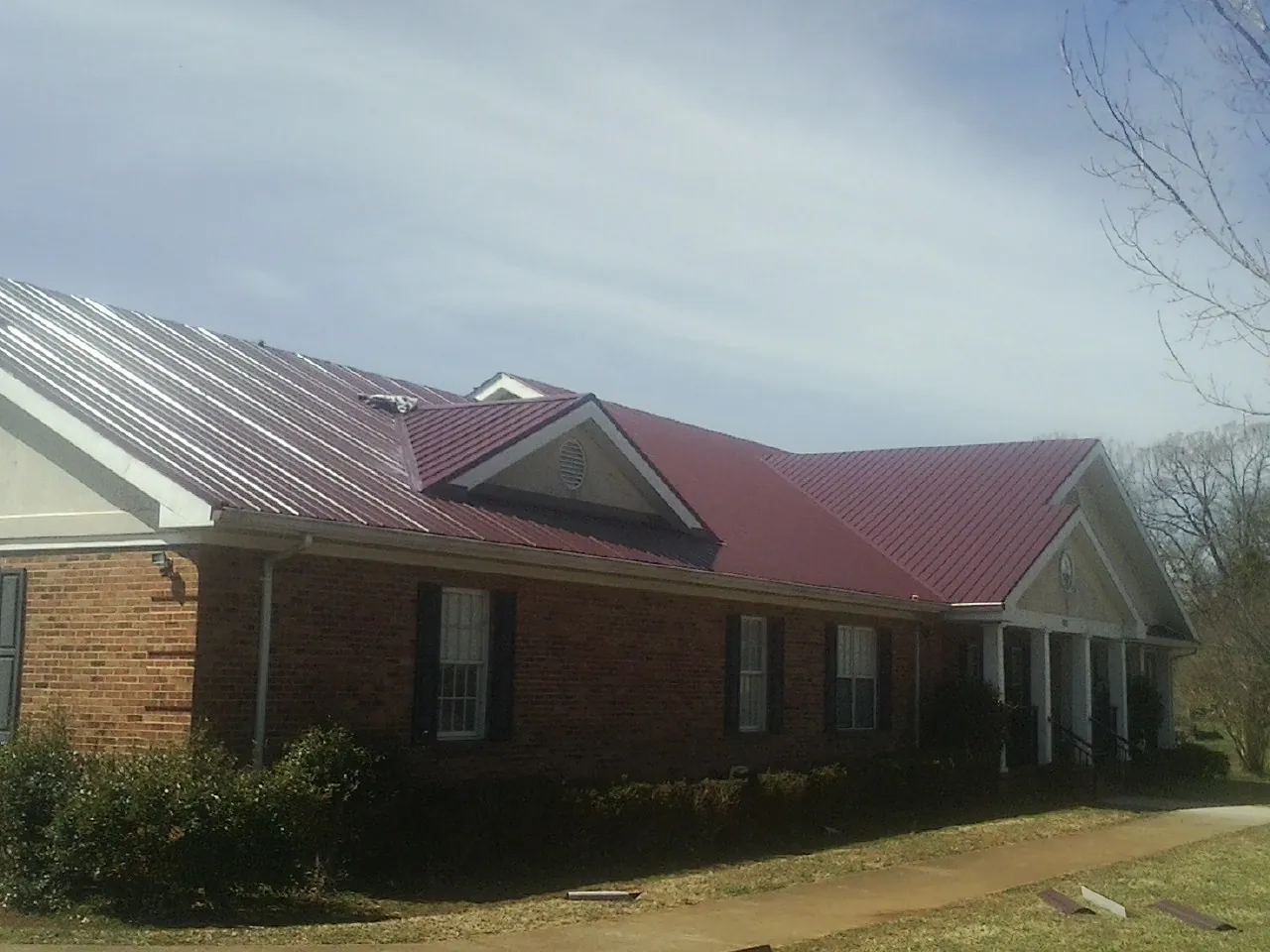 Red metal roof with gabled entries on a long brick building, from a Hail Damage Roof Repair job in Cassville